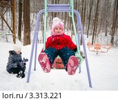 Маленькая весёлая девочка зимой качается на качелях в детском городке зимой (2012 год). Редакционное фото, фотограф Игорь Низов / Фотобанк Лори