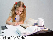 Девочка листает книгу и пишет на листе бумаги конспект сидя за столом (2013 год). Редакционное фото, фотограф Иванов Алексей / Фотобанк Лори