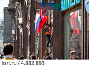 Рабочий украшает флагами фасад здания на Тверской улице города Москвы перед национальным праздником (2013 год). Редакционное фото, фотограф Николай Винокуров / Фотобанк Лори
