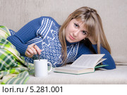 Девушка читает книгу, накрывшись пледом на диване, и с чашкой чая. Стоковое фото, фотограф Иванов Алексей / Фотобанк Лори