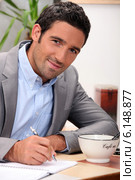 charming 30 years old man dressed in a grey suit and writing in a cosy place. Стоковое фото, фотограф Phovoir Images / Фотобанк Лори