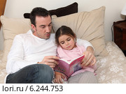 Man reading story to little girl in bed. Стоковое фото, фотограф Phovoir Images / Фотобанк Лори