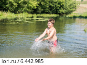Полный десятилетний мальчик брызгается водой, стоя в мелкой реке. Стоковое фото, фотограф Володина Ольга / Фотобанк Лори