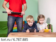 Папа с ремнем в руках стоит на детьми, играющими с мобильными телефонами. Стоковое фото, фотограф Кекяляйнен Андрей / Фотобанк Лори