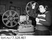 Девушка рассматривает киноплёнку у кинопроектора "Украина". Ретро фотография 1959 года. Редакционное фото, фотограф Евгений Мухортов / Фотобанк Лори