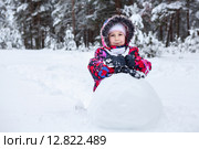 Шестилетняя девочка в зимней одежде катает большой ком снега, стоя на коленях. Стоковое фото, фотограф Кекяляйнен Андрей / Фотобанк Лори
