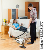 Guy doing house cleaning during girl resting over sofa. Стоковое фото, фотограф Яков Филимонов / Фотобанк Лори