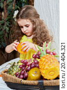 Little girl peels tangerin standing near basket full of fruits. Стоковое фото, фотограф Losevsky Pavel / Фотобанк Лори