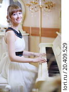 Beautiful girl in white dress plays white piano and looks at camera in light room. Стоковое фото, фотограф Losevsky Pavel / Фотобанк Лори