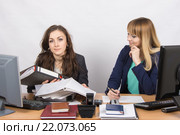 Ситуация в офисе - одна сотрудница завалена работой и смотрит в кадр, другая ничего не делает и с усмешкой смотрит на нее. Стоковое фото, фотограф Иванов Алексей / Фотобанк Лори