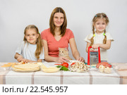 Мама и две маленькие дочки за столом приготавливают ингредиенты для пиццы. За ними наблюдает кошка. Стоковое фото, фотограф Иванов Алексей / Фотобанк Лори