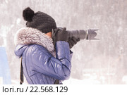 Молодая девушка фотографирует зимой в снежную бурю на зеркальный фотоаппарат с длиннофокусным объективом. Стоковое фото, фотограф Иванов Алексей / Фотобанк Лори