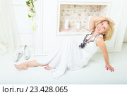 Улыбающаяся молодая женщина в белой летней блузке и длинной белой юбке сидит в гостиной на полу, скинув туфли. Стоковое фото, фотограф Сергей Дубров / Фотобанк Лори
