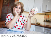 Грустная пенсионерка показывает деньги, сидит за кухонным столом со счетами на оплату. Стоковое фото, фотограф Кекяляйнен Андрей / Фотобанк Лори