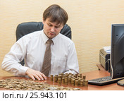 Мужчина в офисе за столом считает монеты и складывает их столбиками. Стоковое фото, фотограф Гетманец Инна / Фотобанк Лори