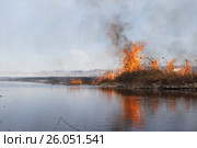 Горит камыш вдоль реки, берег ещё во льду. На заднем плане дома в дыму. Стоковое фото, фотограф Нина Карымова / Фотобанк Лори