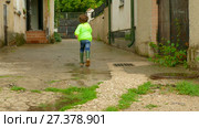The boy in the raincoat runs around the yard in rubber boots. Стоковое видео, видеограф Tatiana Kravchenko / Фотобанк Лори