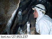 Caver in a white overall looks at the ice formations on the wall of the cave. Стоковое фото, фотограф Евгений Харитонов / Фотобанк Лори