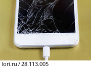 Разбитый смартфон с подключенным кабелем. Сохранение данных перед ремонтом или утилизацией. Золотистый фон. Стоковое фото, фотограф Наталья Гармашева / Фотобанк Лори