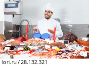 Handsome male chef standing behind icy showcase of fish restaurant, offering fresh seafood. Стоковое фото, фотограф Яков Филимонов / Фотобанк Лори