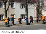 Рабочие маляры в спецодежде ЖКХ весной красят забор, дорожное ограждение на фоне дома и дороги (2018 год). Редакционное фото, фотограф Илья Илмарин / Фотобанк Лори