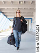 Portrait of young cheerful female traveler wearing casual clothes carrying heavy backpack and luggage at airport. Стоковое фото, фотограф Matej Kastelic / Фотобанк Лори