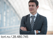 Cheerful serious young businessman standing in urban surrounding with arms crossed. Стоковое фото, фотограф Kirill Kedrinskiy / Ingram Publishing / Фотобанк Лори