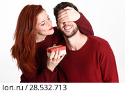 Young woman giving a gift to his man. Beautiful couple dressed in red on white background. Redhead girl. Стоковое фото, фотограф Javier Sánchez Mingorance / Ingram Publishing / Фотобанк Лори