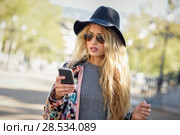 Young woman looking at her smartphone in urban background. Girl wearing jacket, hat, sweater and sunglasses. Стоковое фото, фотограф Javier Sánchez Mingorance / Ingram Publishing / Фотобанк Лори