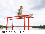 Улыбающаяся девочка подросток выполняет физическое упражнение на брусьях. На заднем плане - река Иртыш,центральная часть  г.Омска. Стоковое фото, фотограф Круглов Олег / Фотобанк Лори