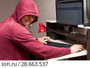 Интернет тролль у компьютера. Агрессивный молодой человек с дьявольской усмешкой пишет гадости в сети интернет. Стоковое фото, фотограф Лариса Капусткина / Фотобанк Лори