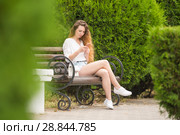 Молодая девушка общается в социальных сетях, сидя на скамейке в парке. Стоковое фото, фотограф Иванов Алексей / Фотобанк Лори