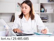 Practicioner girl in medical uniform is working with documents and laptop. Стоковое фото, фотограф Яков Филимонов / Фотобанк Лори