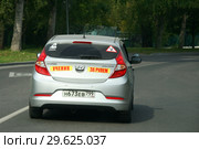 "Ученик за рулем". Учебный автомобиль едет по улице в городе (Hyundai Solaris). Наклейка "Ребенок в машине" на заднем стекле (2018 год). Редакционное фото, фотограф Щеголева Ольга / Фотобанк Лори