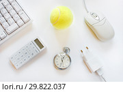 Компьютерная клавиатура, калькулятор, мышь, телефонная зарядка, секундомер и теннисный желтый мяч на светлом фоне. Стоковое фото, фотограф Юрий Морозов / Фотобанк Лори