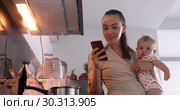 Woman holds baby her arms simultaneously looks into phone. Стоковое видео, видеограф Ekaterina Demidova / Фотобанк Лори