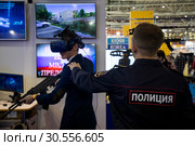 Сотрудник полиции помогает посетителю на тренажере виртуальной реальности для спецслужб на стенде Нижегородской академии МВД на Московском международном салоне образования на ВДНХ ЭКСПО в городе Москве, Россия (2019 год). Редакционное фото, фотограф Николай Винокуров / Фотобанк Лори