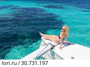 Woman relaxing on a summer sailing cruise, sitting on a luxury catamaran near picture perfect white sandy beach on Spargi island in Maddalena Archipelago, Sardinia, Italy. Стоковое фото, фотограф Matej Kastelic / Фотобанк Лори