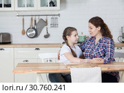 Adult mom has a serious conversation with her teenage daughter, talking at kitchen at table, copyspace. Стоковое фото, фотограф Кекяляйнен Андрей / Фотобанк Лори