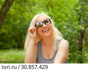 Портрет счастливой девушки на фоне зелени  в смешных солнечных очках с одним стеклом и отражением в нем загородного домика. Стоковое фото, фотограф Элина Гаревская / Фотобанк Лори