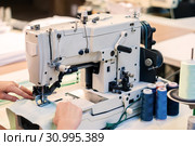 Industrial overlock sewing machine and hands of seamstress at work in the garment factory. Стоковое фото, фотограф Евгений Харитонов / Фотобанк Лори