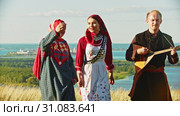 People in traditional russian clothes walking on the field and singing a song - a man playing balalaika. Стоковое видео, видеограф Константин Шишкин / Фотобанк Лори