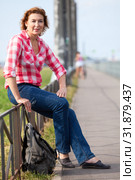 Portrait of mature Caucasian woman in red t-shirt and bluse jeans sitting with backpack on streets. Стоковое фото, фотограф Кекяляйнен Андрей / Фотобанк Лори
