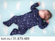One month old infant sleeping in bed with hands up, dark blue clothes, light blue linen with clouds, full length. Стоковое фото, фотограф Кекяляйнен Андрей / Фотобанк Лори