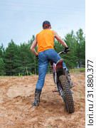 Riding motorcross motorcycle in sandy pit, Caucasian man dressed orange t-shirt standing with bike, rear view. Стоковое фото, фотограф Кекяляйнен Андрей / Фотобанк Лори