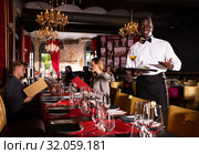Hospitable african-american waiter standing with serving tray meeting restaurant guests. Стоковое фото, фотограф Яков Филимонов / Фотобанк Лори