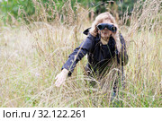 Mature woman looks through binoculars in high grass, bird watcher, copy space. Стоковое фото, фотограф Кекяляйнен Андрей / Фотобанк Лори