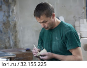 Мастер в цеху вручную обрабатывает статуэтку из фарфора. Фарфоровая фабрика "Фарфор Вербилок",  Московская область (2019 год). Редакционное фото, фотограф Наталья Николаева / Фотобанк Лори