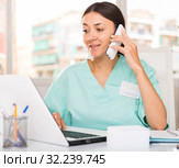 Practicioner woman in medical uniform talking by phone at laptop. Стоковое фото, фотограф Яков Филимонов / Фотобанк Лори