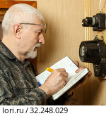 The man takes the readings of the apartment electric meter and writes it in the notebook. Стоковое фото, фотограф Акиньшин Владимир / Фотобанк Лори